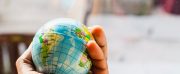 A hand holding a small globe with geographical details visible.