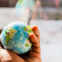 A hand holding a small globe with geographical details visible.