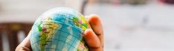 A hand holding a small globe with geographical details visible.