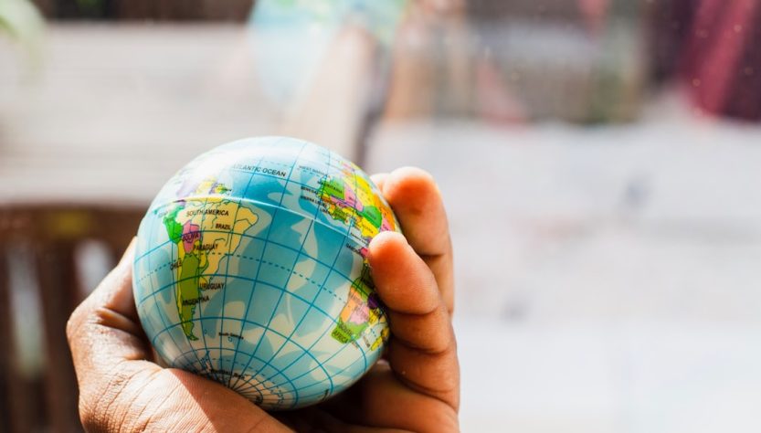 A hand holding a small globe with geographical details visible.