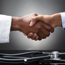 Close-up of two hands shaking with a stethoscope nearby