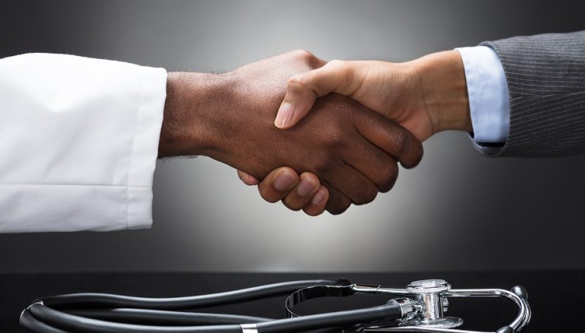 Close-up of two hands shaking with a stethoscope nearby